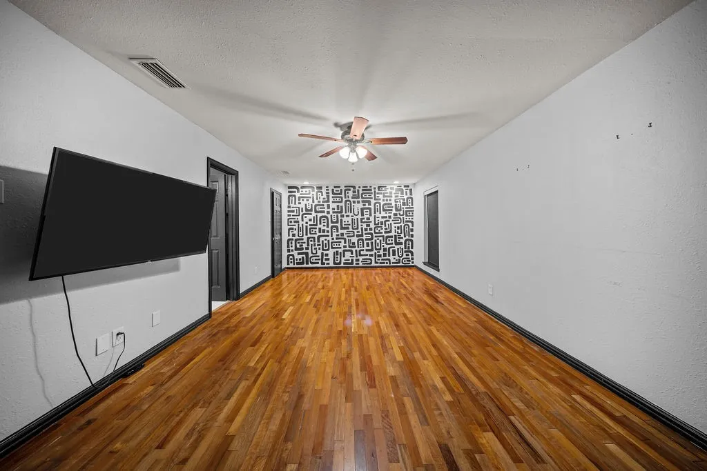 Wood-finish flooring with a ceiling fan and recessed lighting