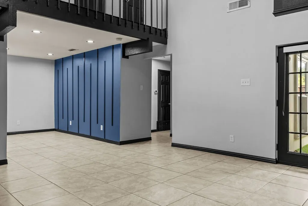 Two-story ceiling, tile flooring, accent wall with vertical paneling, recessed lighting, and a glass-paneled exterior door