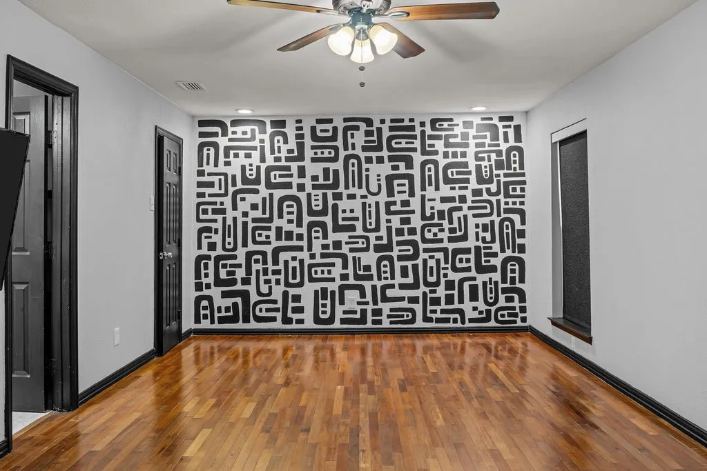 Wood-finish flooring, a decorative accent wall, a ceiling fan with integrated lighting, and dark trim details