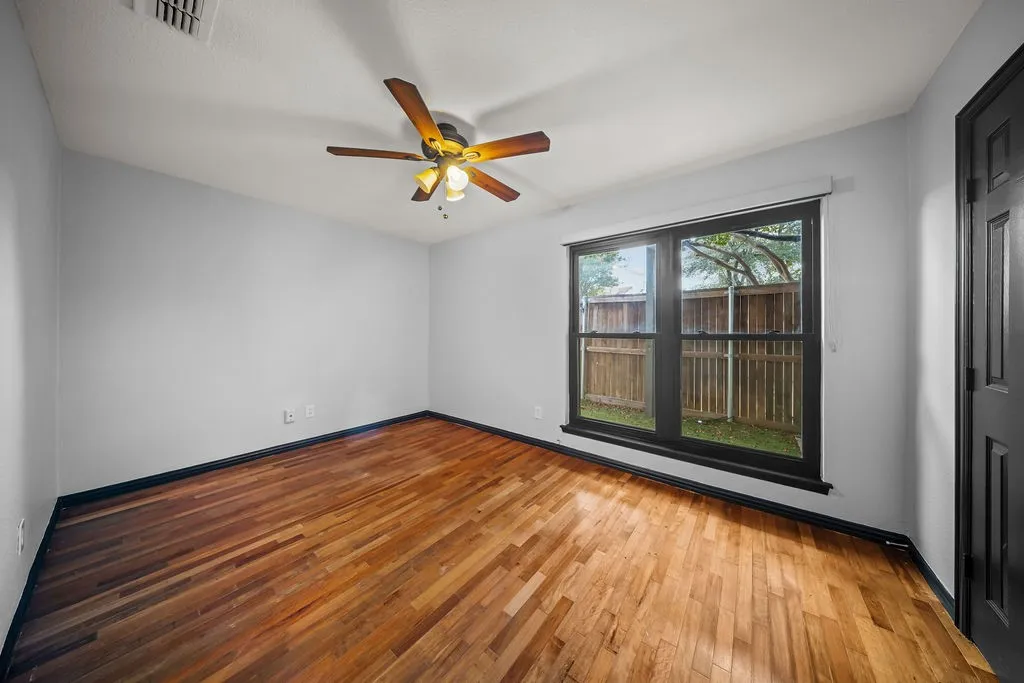 Wood-finish flooring, ceiling fan with integrated lighting, window with black trim, white walls, and a paneled door