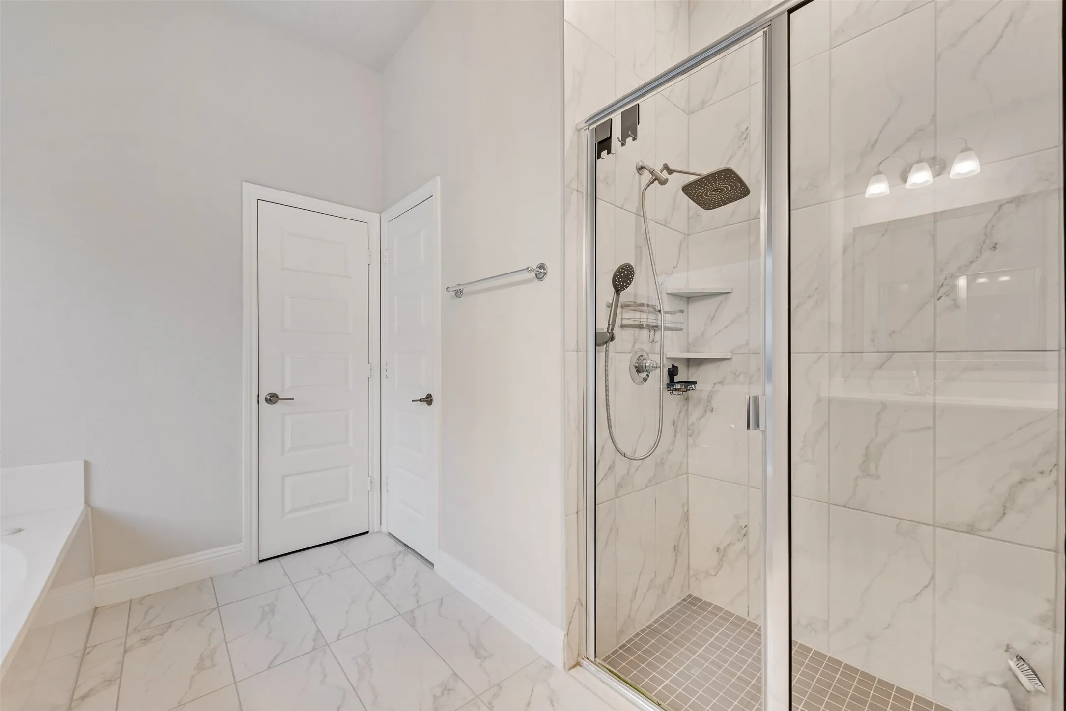 Glass-enclosed shower with a rainfall showerhead, handheld sprayer, built-in shelving, and a tiled floor