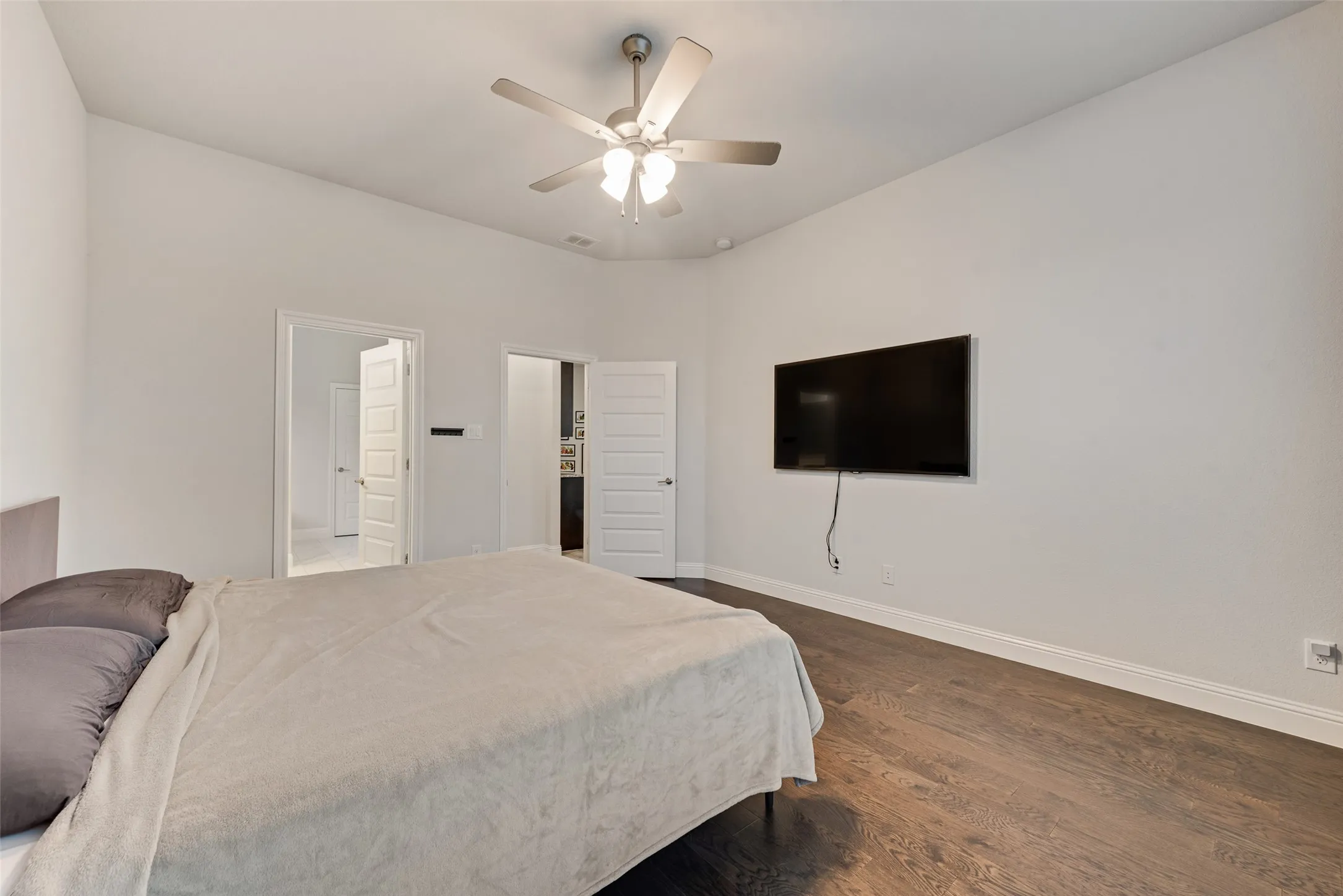 Vaulted ceiling with an attached ceiling fan, wood-finish flooring, and white paneled doors