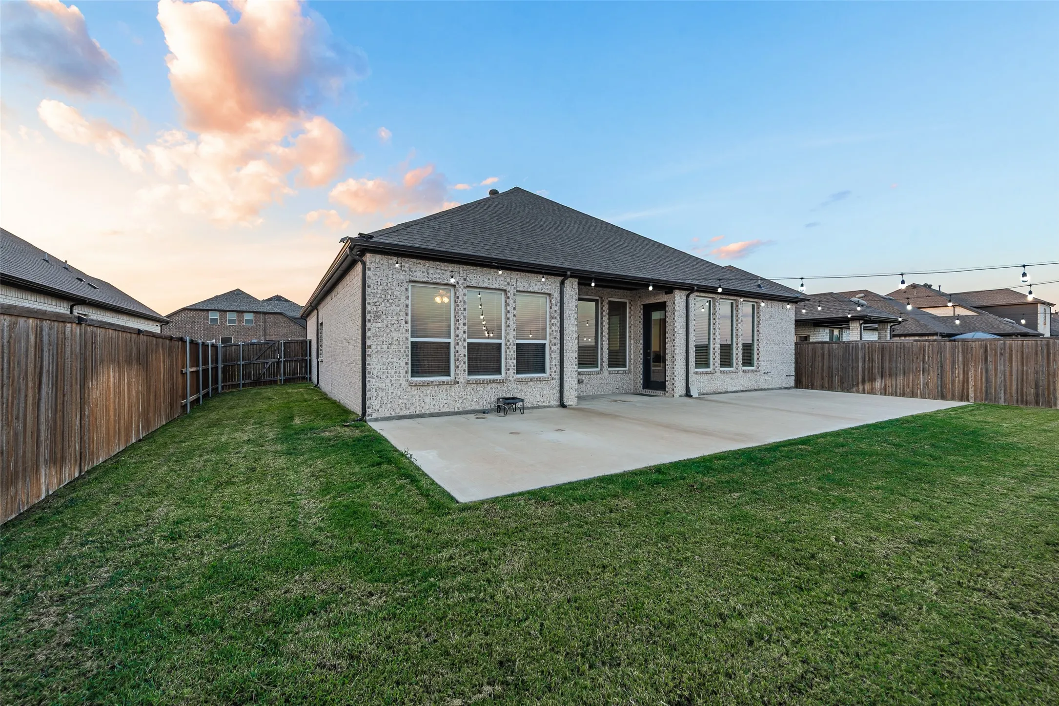 Expansive backyard featuring a manicured lawn, a large concrete patio, and a brick exterior