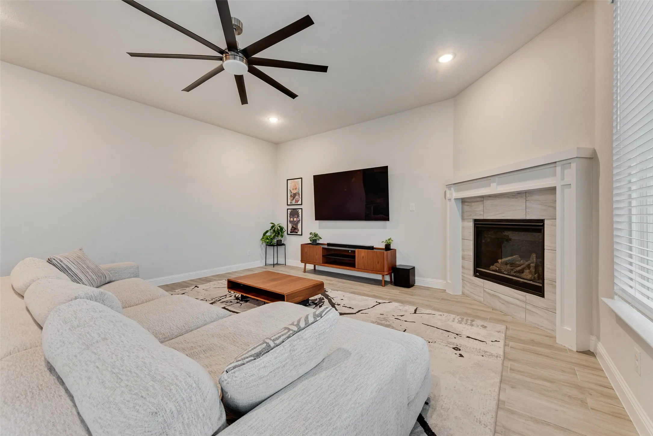Vaulted ceiling with a contemporary ceiling fan, recessed lighting, corner fireplace with tile surround, and light wood-finish flooring