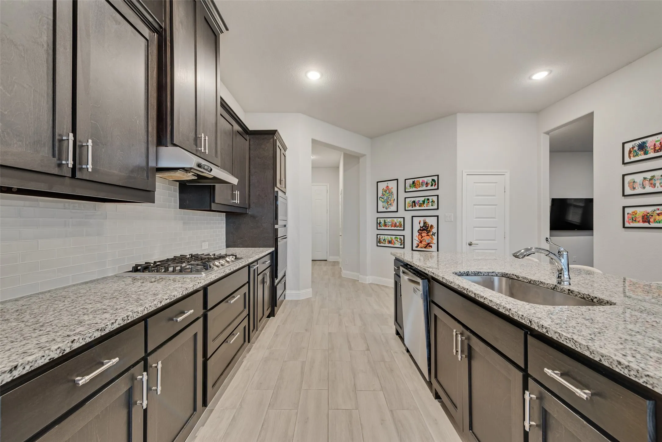 Kitchen featuring dark wood-finish cabinetry, light-toned countertops, a built-in gas range with a vent hood, a stainless steel sink, and wood-finish flooring