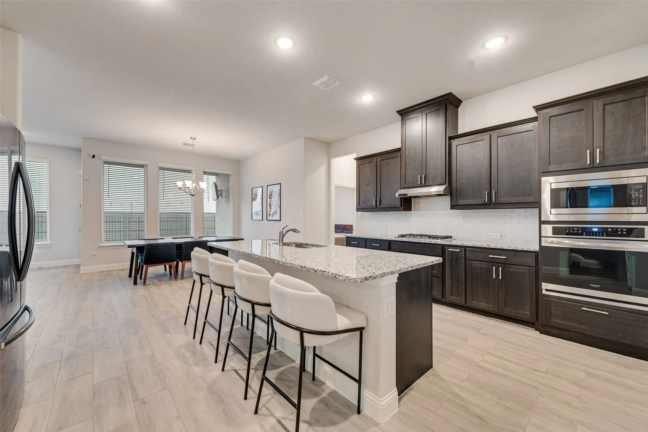 Open concept kitchen with wood-finish flooring, dark wood cabinetry, stainless steel appliances, a center island with a light-colored countertop, and recessed lighting