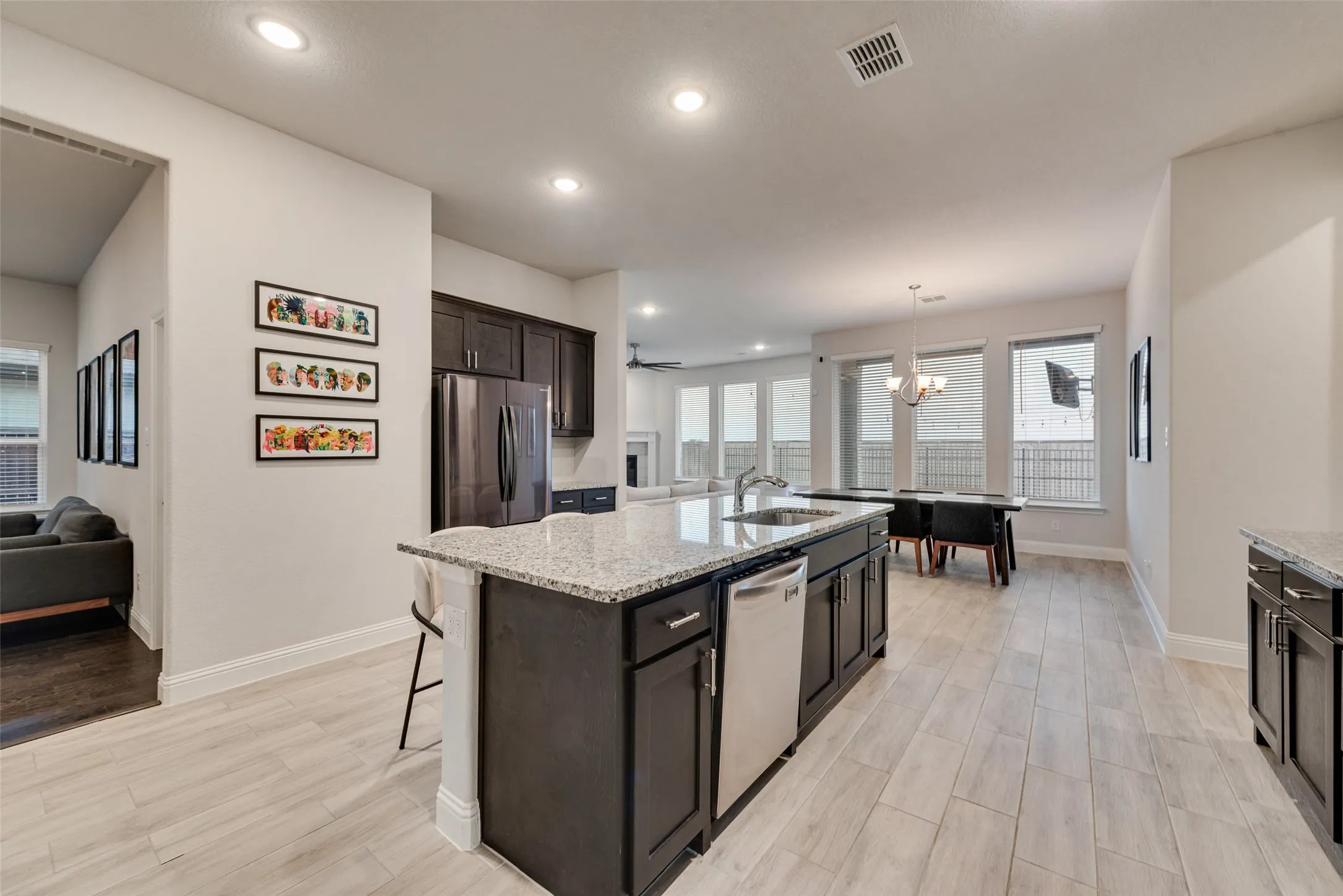 Expansive kitchen island with a granite countertop and integrated sink, dark wood cabinetry, stainless steel dishwasher, and recessed lighting