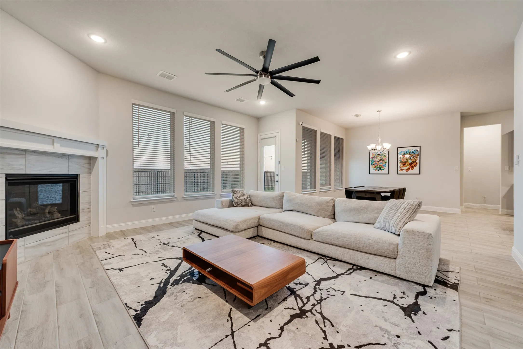 Spacious living area featuring wood-finish flooring, a tiled fireplace with a mantel, and multiple large windows