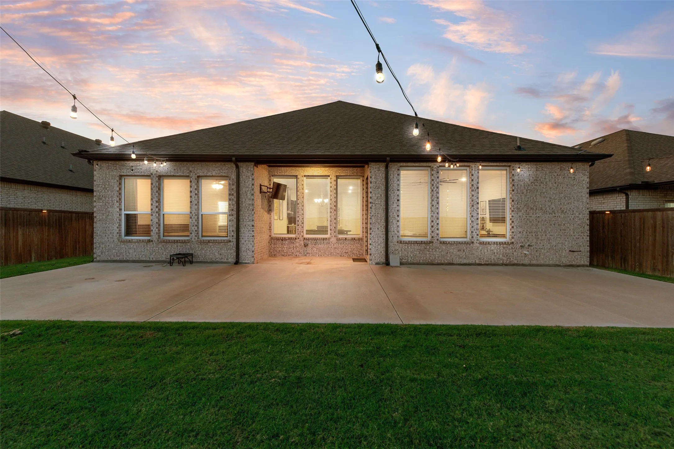 Expansive concrete patio with string lighting and a brick exterior