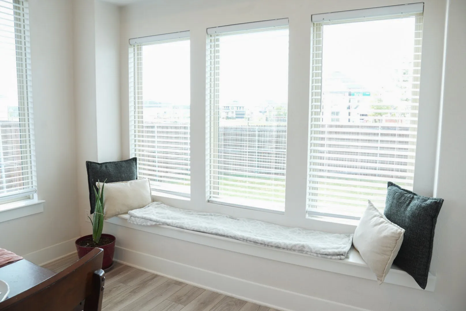 Built-in window bench with three large windows, featuring white blinds and light wood-finish flooring