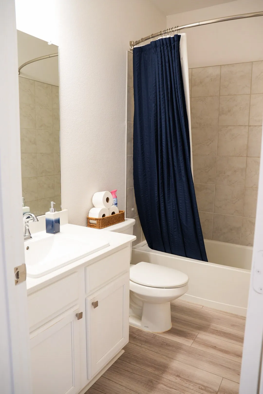 White vanity with integrated sink, wood-finish flooring, tiled shower surround, and a full-size bathtub