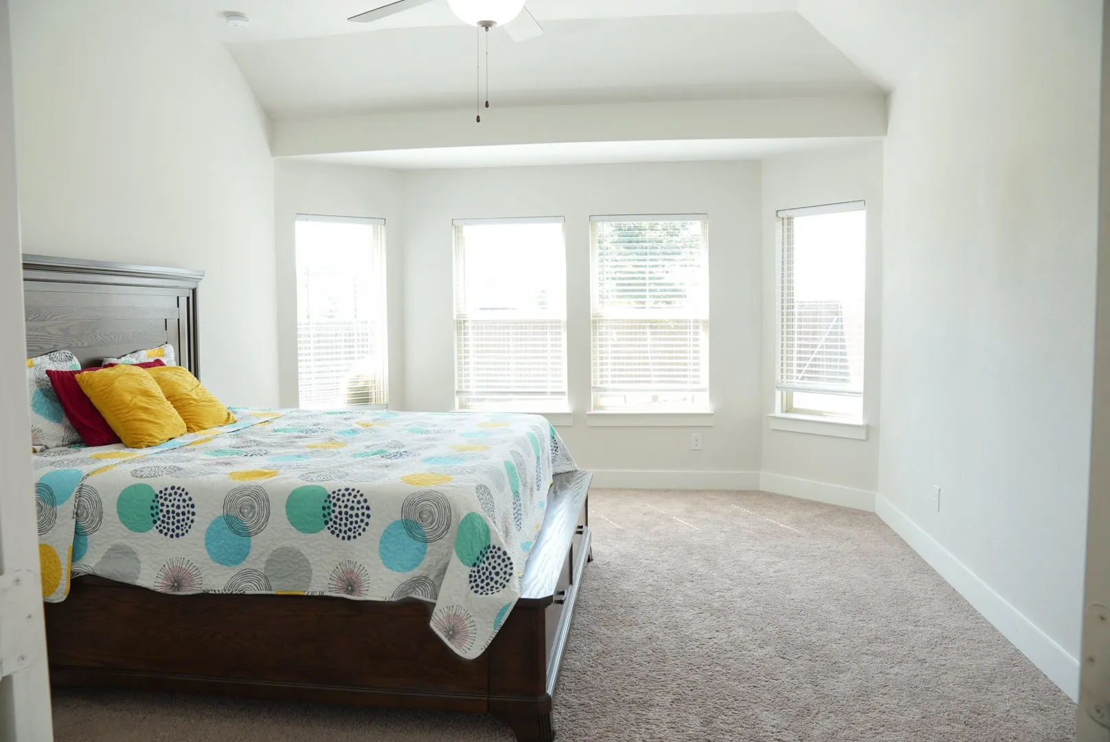 Vaulted ceiling with ceiling fan, bay window with multiple windows, carpet flooring, and white walls