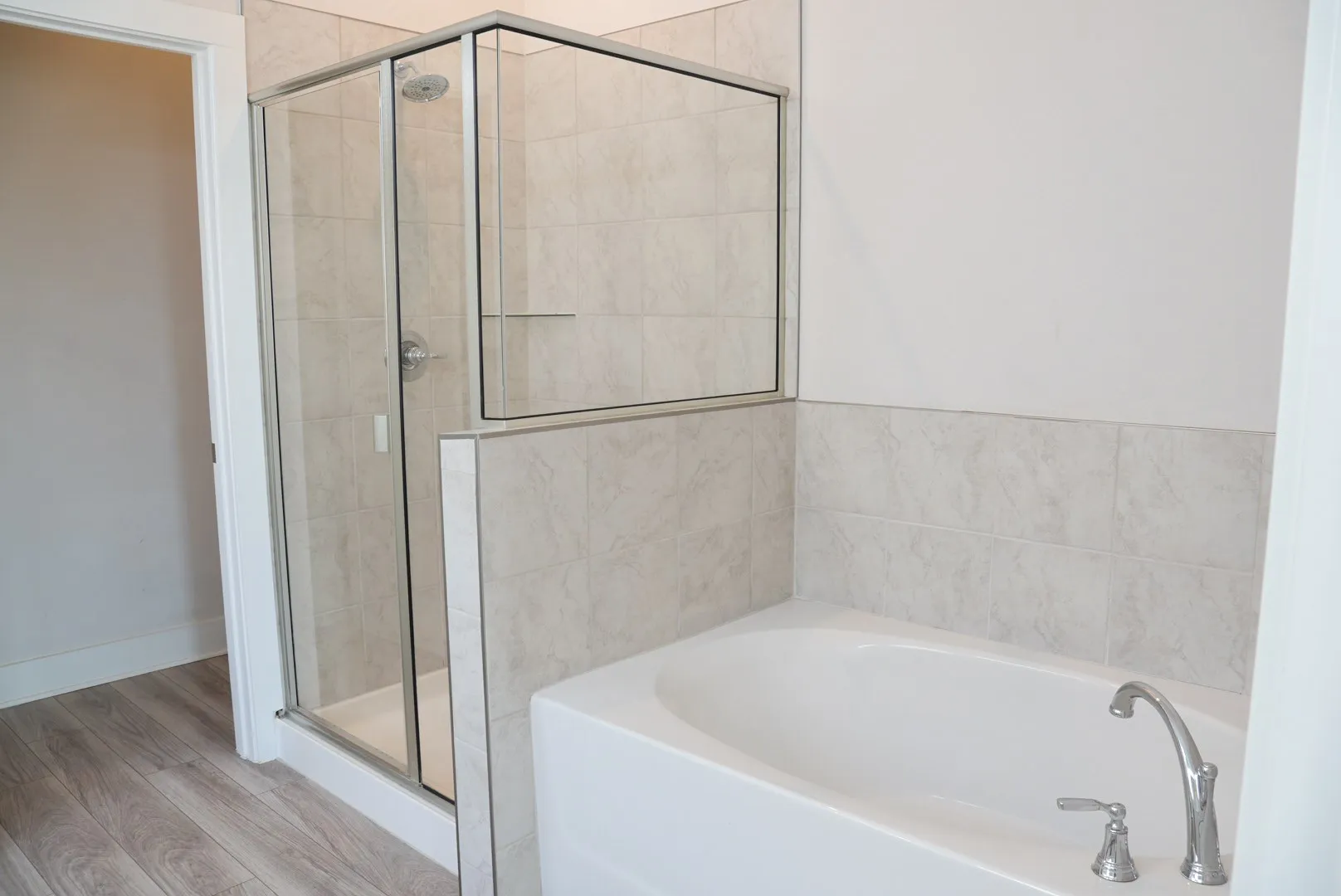 Glass-enclosed shower, tiled shower surround, soaking tub with deck-mounted faucet, and wood-finish flooring