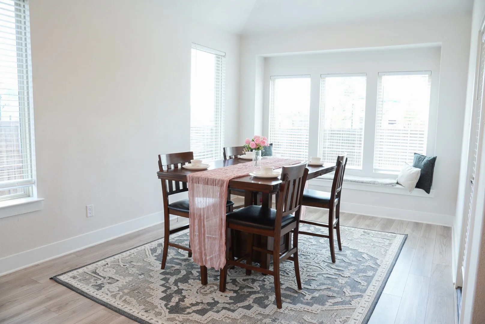 Expansive room featuring wood-finish flooring, a built-in window seat, and multiple large windows with blinds
