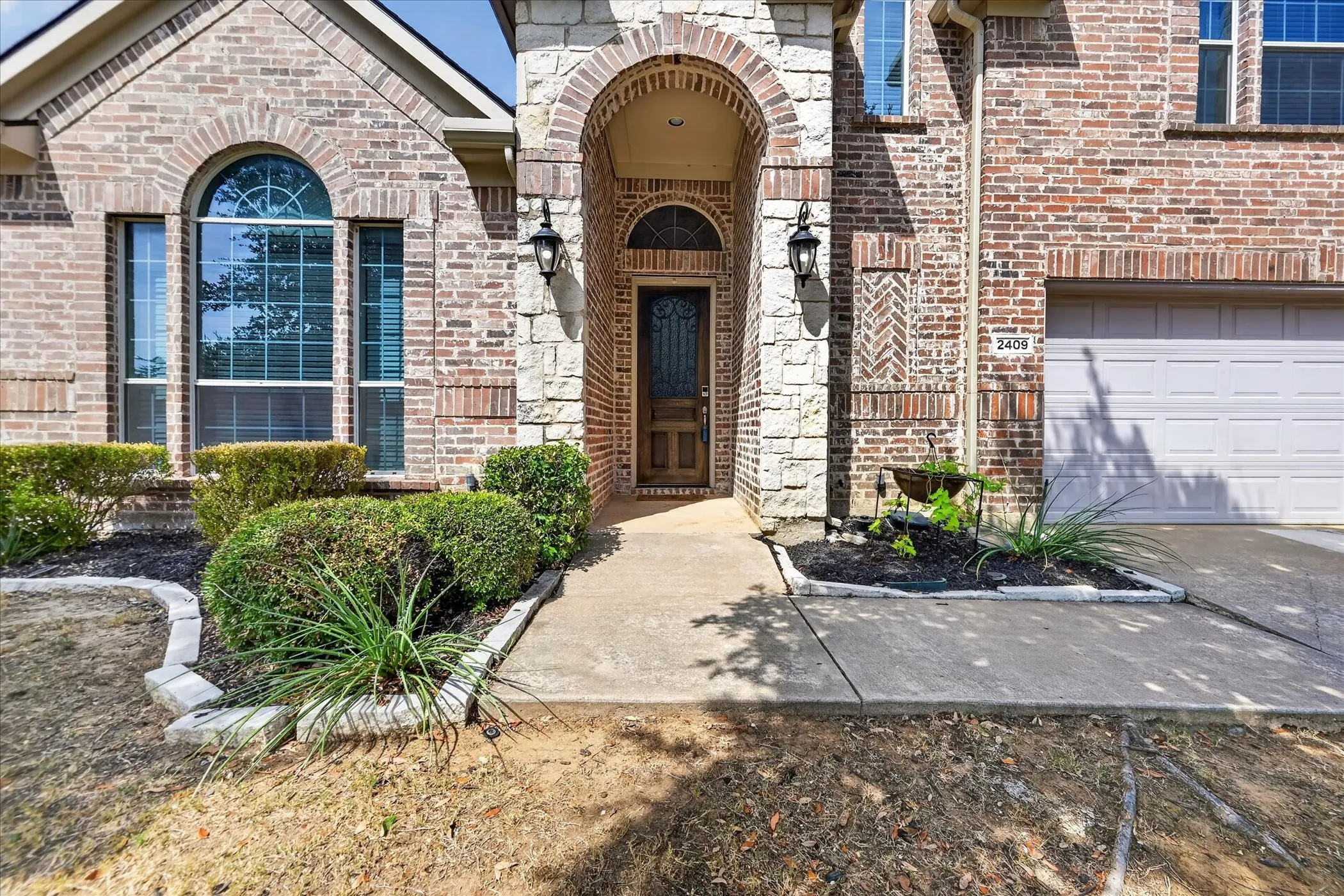 Elegant brick exterior with arched entryway featuring solid wood door, decorative wall sconces, and architectural detailing