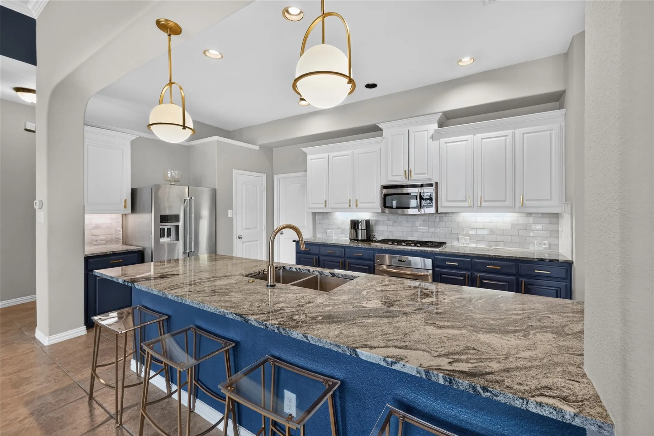 Kitchen featuring an expansive island with a double basin sink, stainless steel appliances, white upper cabinetry, and blue lower cabinetry