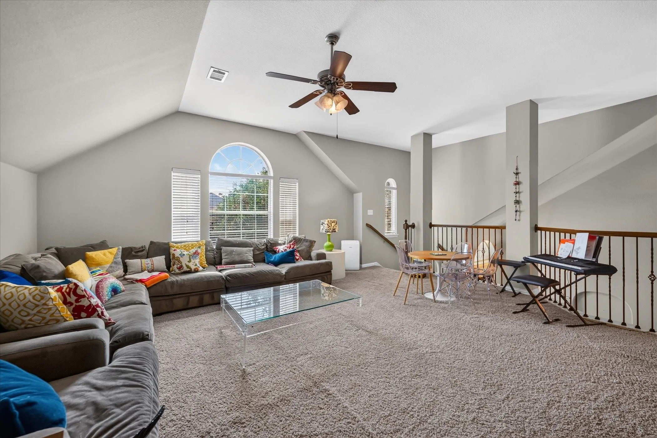 Vaulted ceiling with ceiling fan, arched transom window, carpet flooring, and wrought iron railing