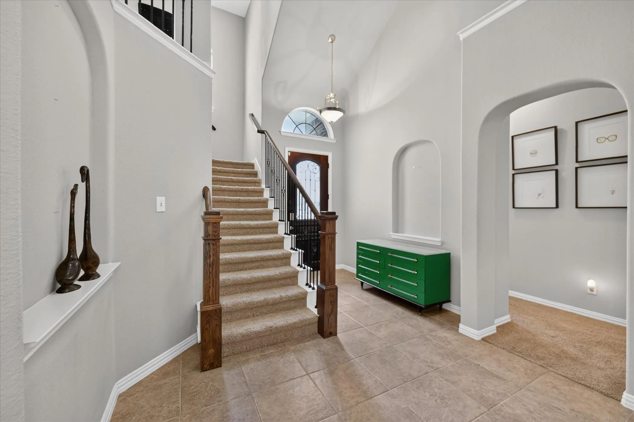Vaulted entryway featuring tile flooring, a carpeted staircase with wood newel posts and wrought iron balusters, and an arched niche