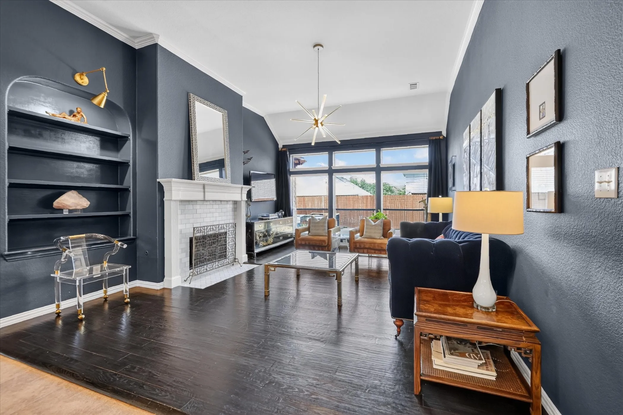 Spacious living area featuring dark wood-finish flooring, a white mantel fireplace with tile surround, built-in shelving, and large windows