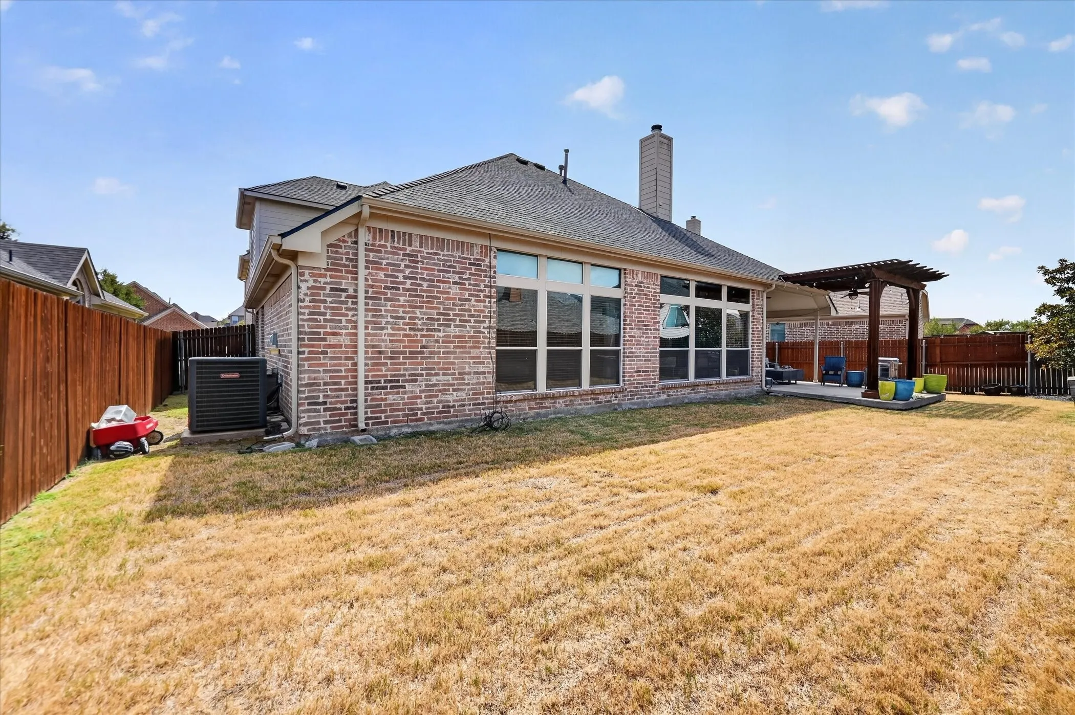 Brick exterior with a gabled roof, a covered patio, a wood pergola, and a privacy fence