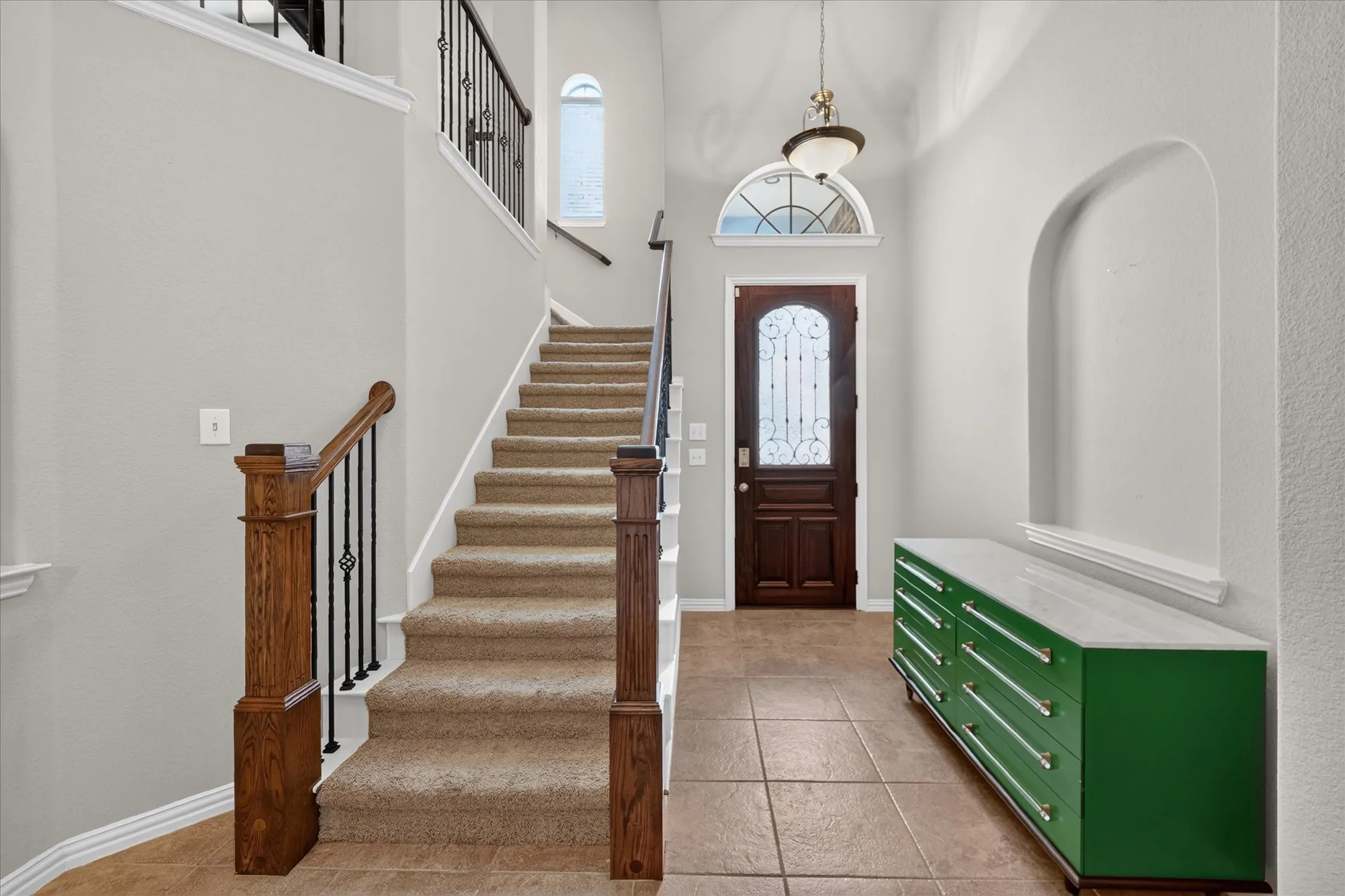 Two-story entry with a dark wood front door, arched transom window, and tiled flooring
