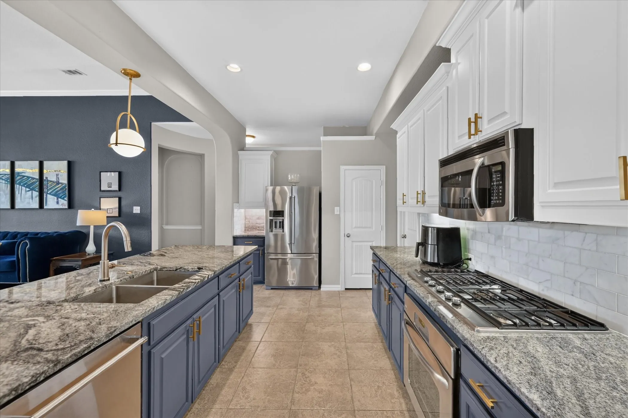 Kitchen featuring dark blue lower cabinetry, white upper cabinetry, stainless steel appliances, a double basin sink, and tile flooring