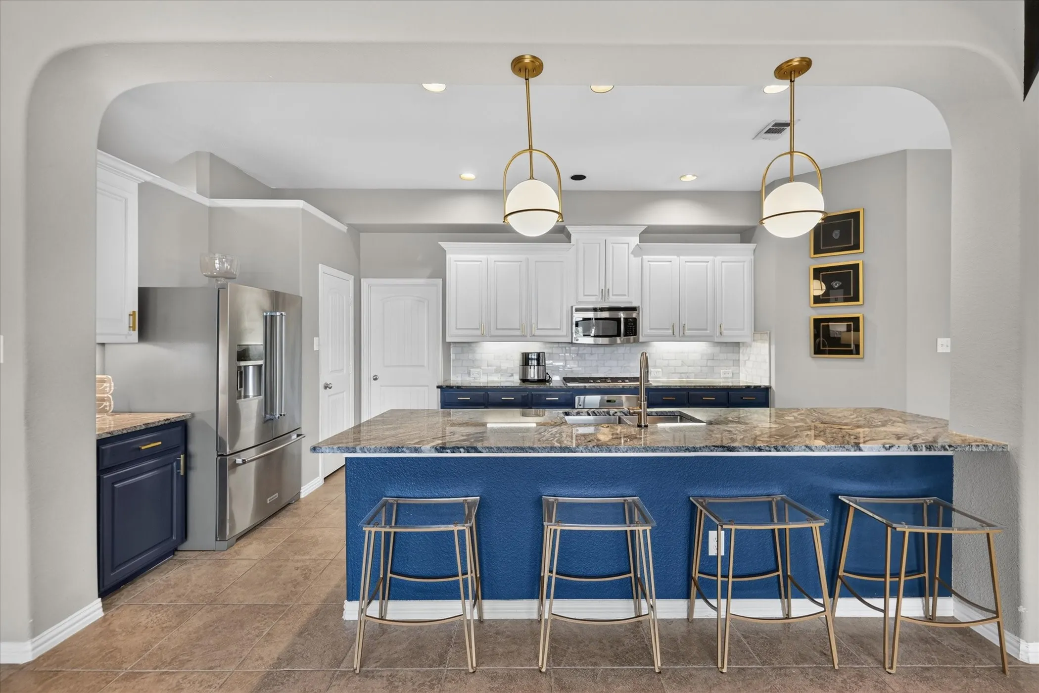 Kitchen featuring an expansive island with a stone countertop, white upper cabinetry, blue lower cabinetry, stainless steel appliances, and tile flooring