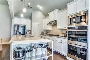 Kitchen featuring white cabinetry, stainless steel appliances, a center island with countertop seating, and a vaulted ceiling