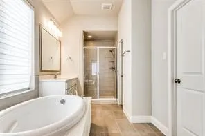 Freestanding oval bathtub, glass-enclosed shower, single vanity with under-sink storage, framed mirror, and tile flooring