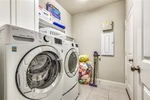 Modern laundry room featuring side-by-side front-load washer and dryer with stacked storage shelving above, tile flooring, and ample counter space for folding and sorting