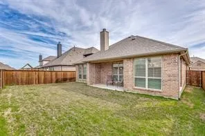 Expansive backyard featuring a privacy fence, covered patio, multiple windows, and a brick exterior