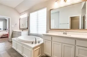 Soaking tub with white paneling, dual vanities with white cabinetry, large vanity mirror, and overhead lighting fixtures