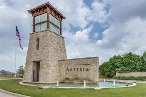 Stone-clad entrance tower with an upper windowed section, featuring a multi-tiered roofline, a prominent "ARTESIA" sign, and a circular fountain with multiple water jets