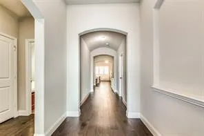 Long hall with arched entryways, wood-finish flooring, and crown molding