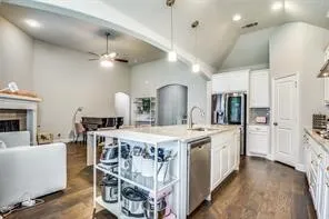 Vaulted ceiling with recessed lighting, wood-finish flooring, white kitchen cabinetry, center island with undermount sink, and stainless steel appliances