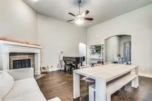 Vaulted ceiling, hardwood flooring, fireplace with white mantel, arched doorway, and a ceiling fan