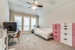 Neutral-toned carpeting, vaulted ceiling, and three windows with white plantation shutters