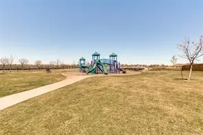 Expansive outdoor play area featuring a multi-level structure with slides, a surrounding grassy field, and a paved pathway