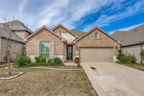 Brick and stone facade, attached two-car garage, mature landscaping, concrete driveway, and covered entryway