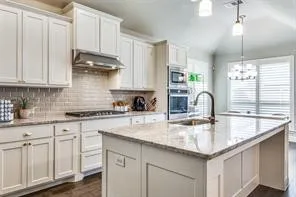 Gourmet kitchen featuring white cabinetry, stone countertops, a subway tile backsplash, a gas cooktop with stainless steel hood, and built-in double ovens