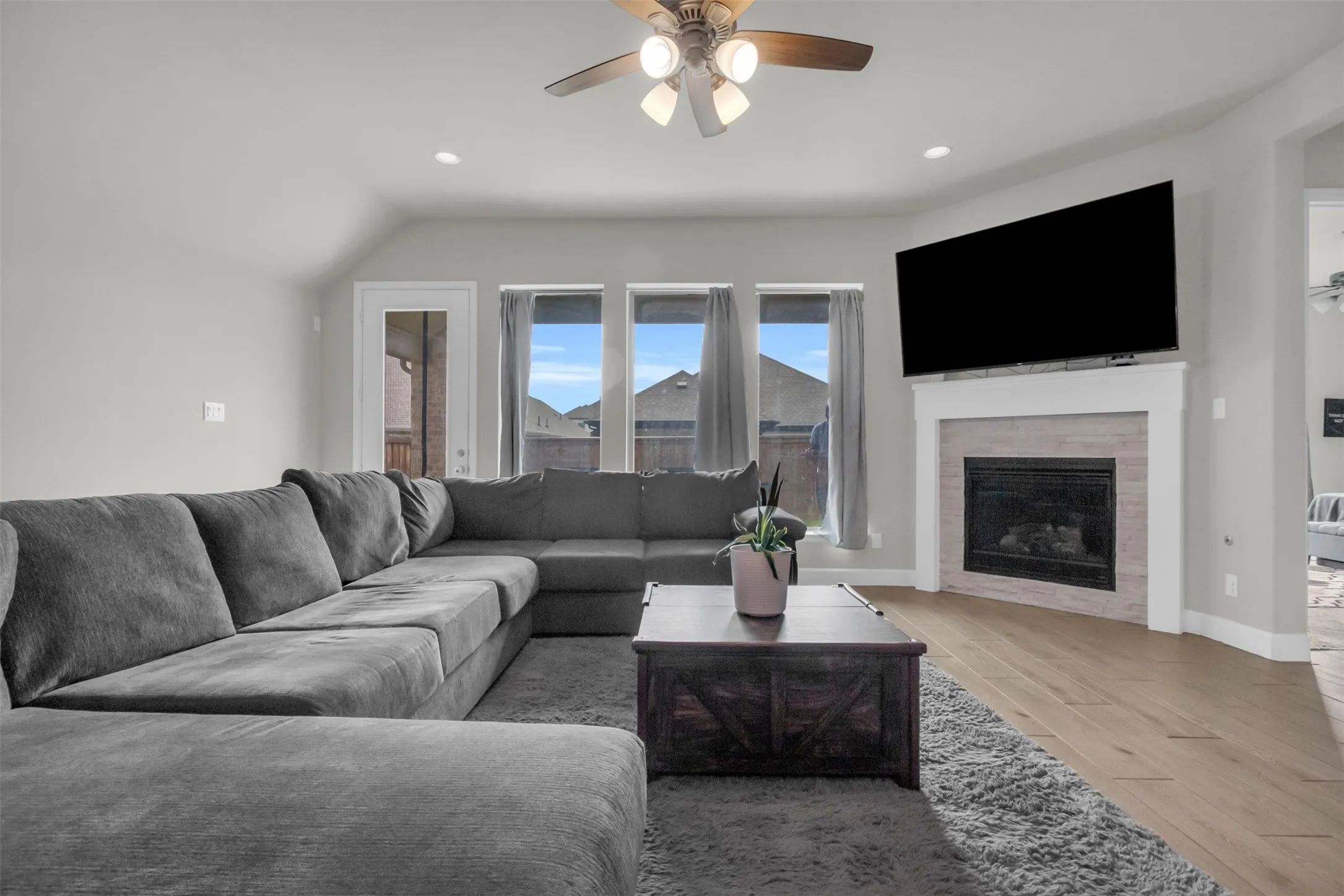 Living room with light wood finished floors, a glass covered fireplace, a ceiling fan, recessed lighting, and vaulted ceiling