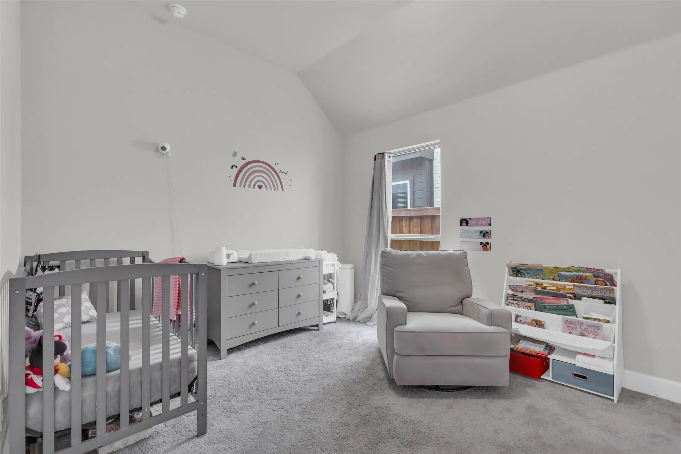 Carpeted bedroom featuring a crib and lofted ceiling