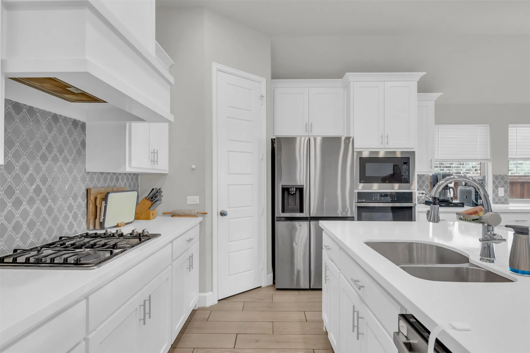 Kitchen with backsplash, white cabinets, stainless steel appliances, wood finish floors, and custom range hood