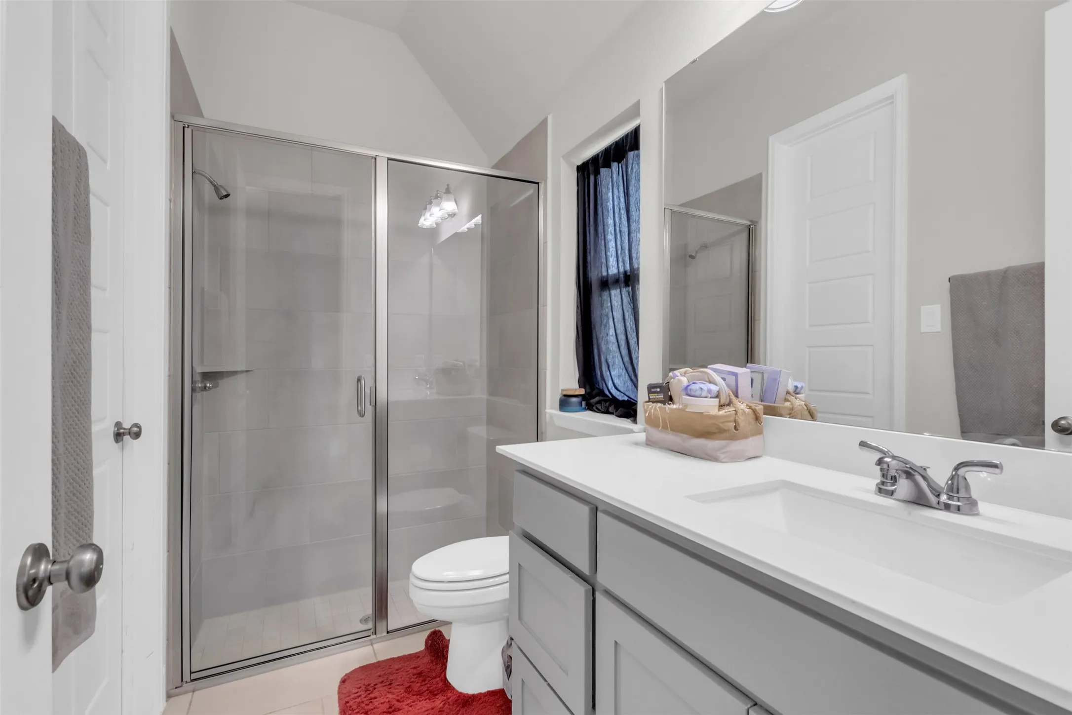 Full bathroom with a stall shower, vanity, light tile patterned flooring, and vaulted ceiling