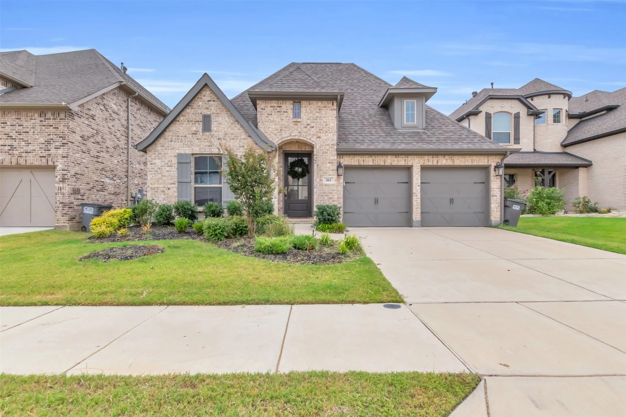French country home with brick siding, an attached garage, roof with shingles, and concrete driveway