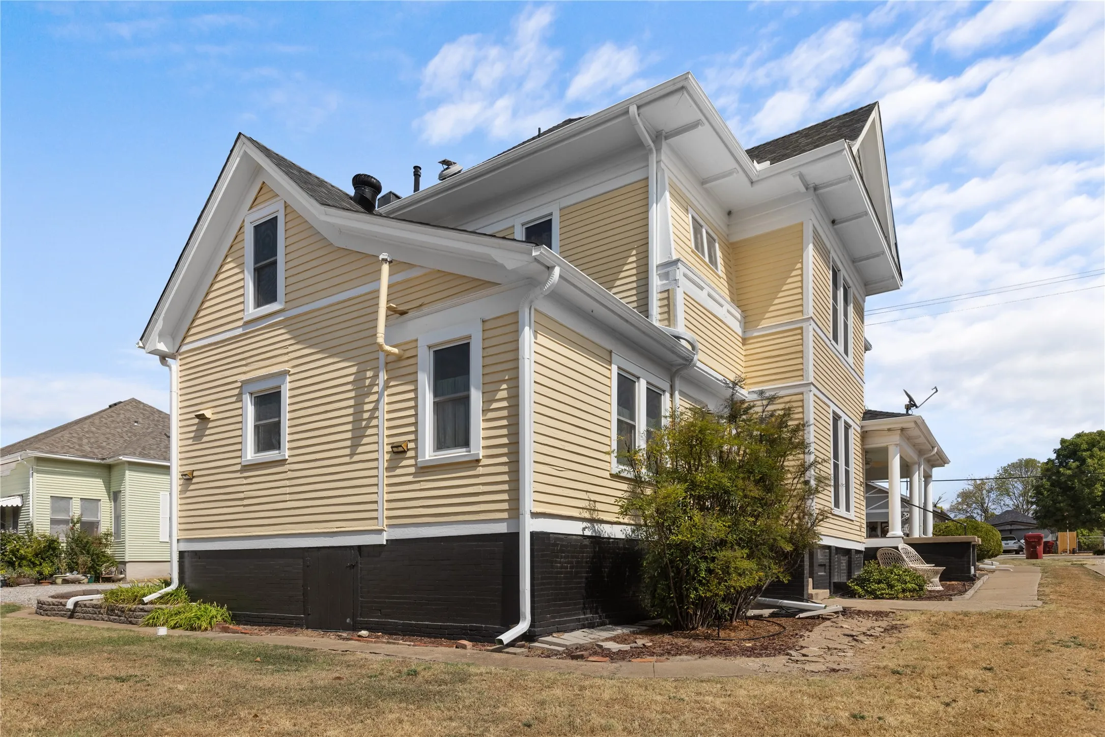 Exterior with yellow siding and white trim, featuring multiple windows, a gabled roofline, and a dark foundation