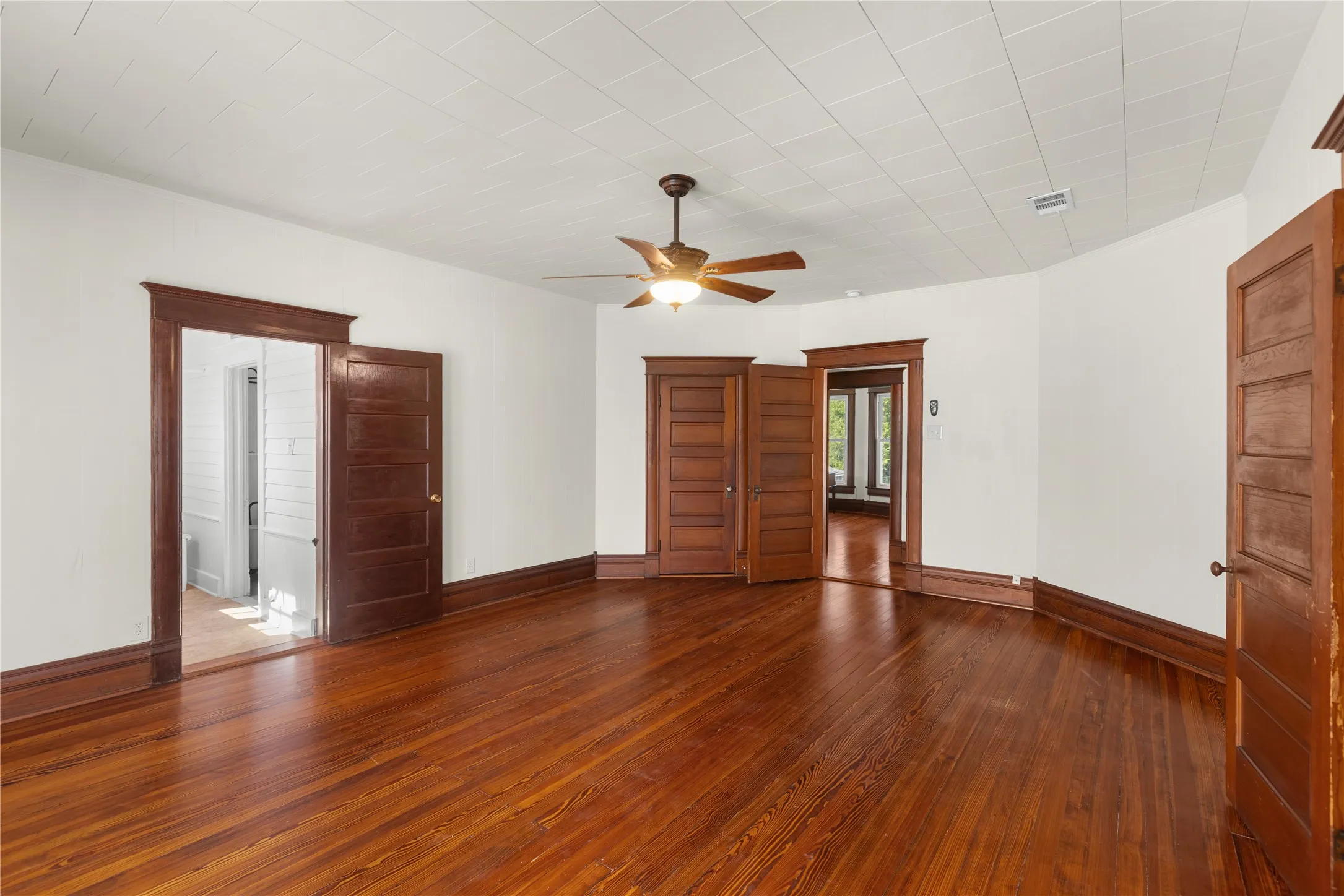 Hardwood flooring, wood-paneled doors, wood trim, ceiling fan, and white walls