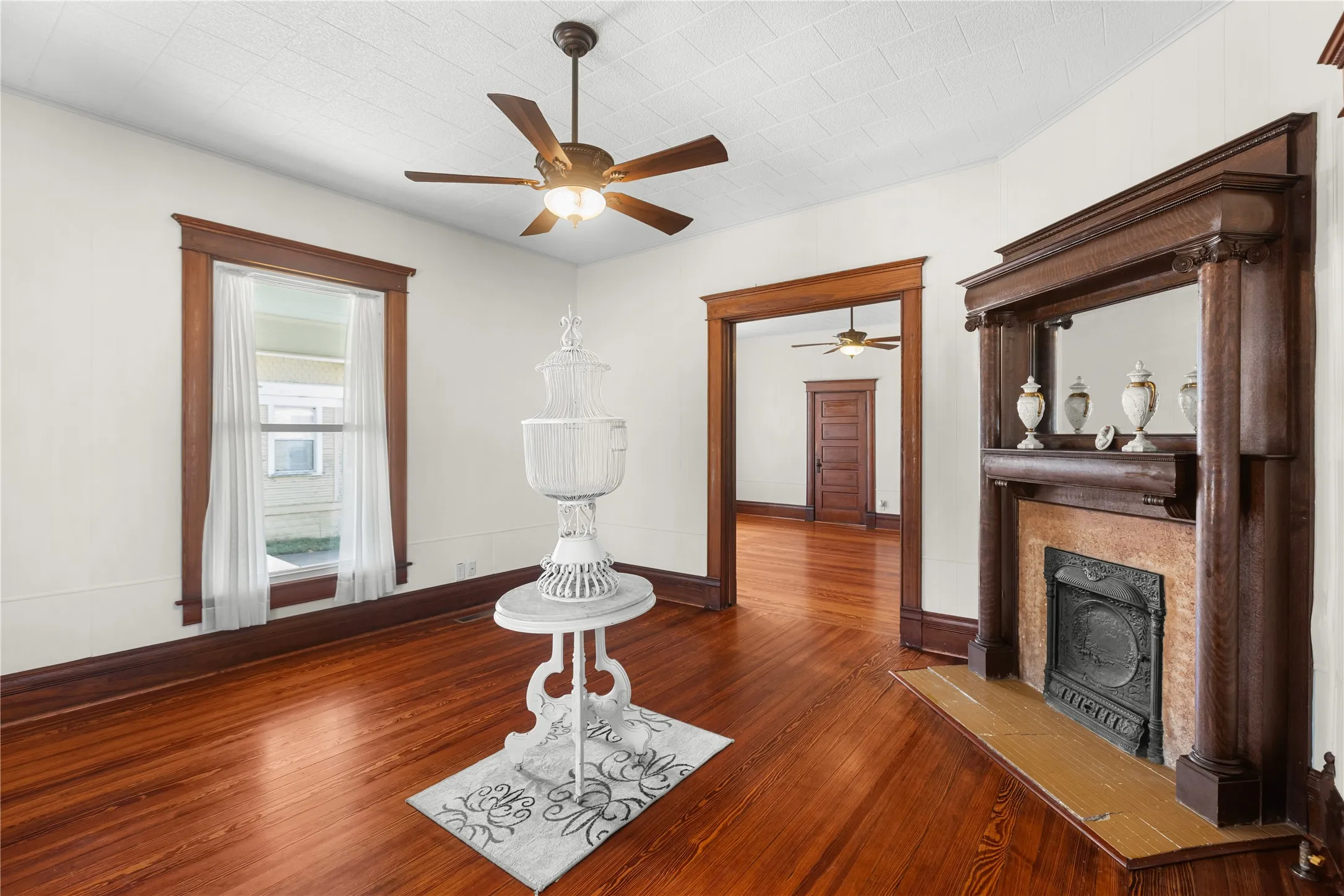 Wood-finish flooring, ornate wood-trimmed fireplace, ceiling fan with integrated lighting, wood window trim, and wood door frames