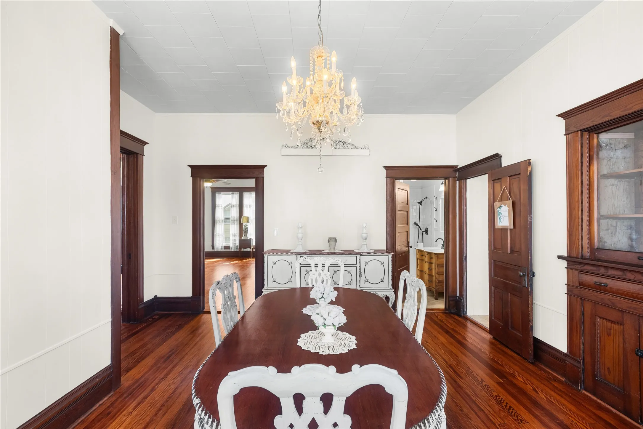 Polished wood-finish flooring, ornate chandelier, decorative trim, white paneled ceilings, and built-in wood cabinetry