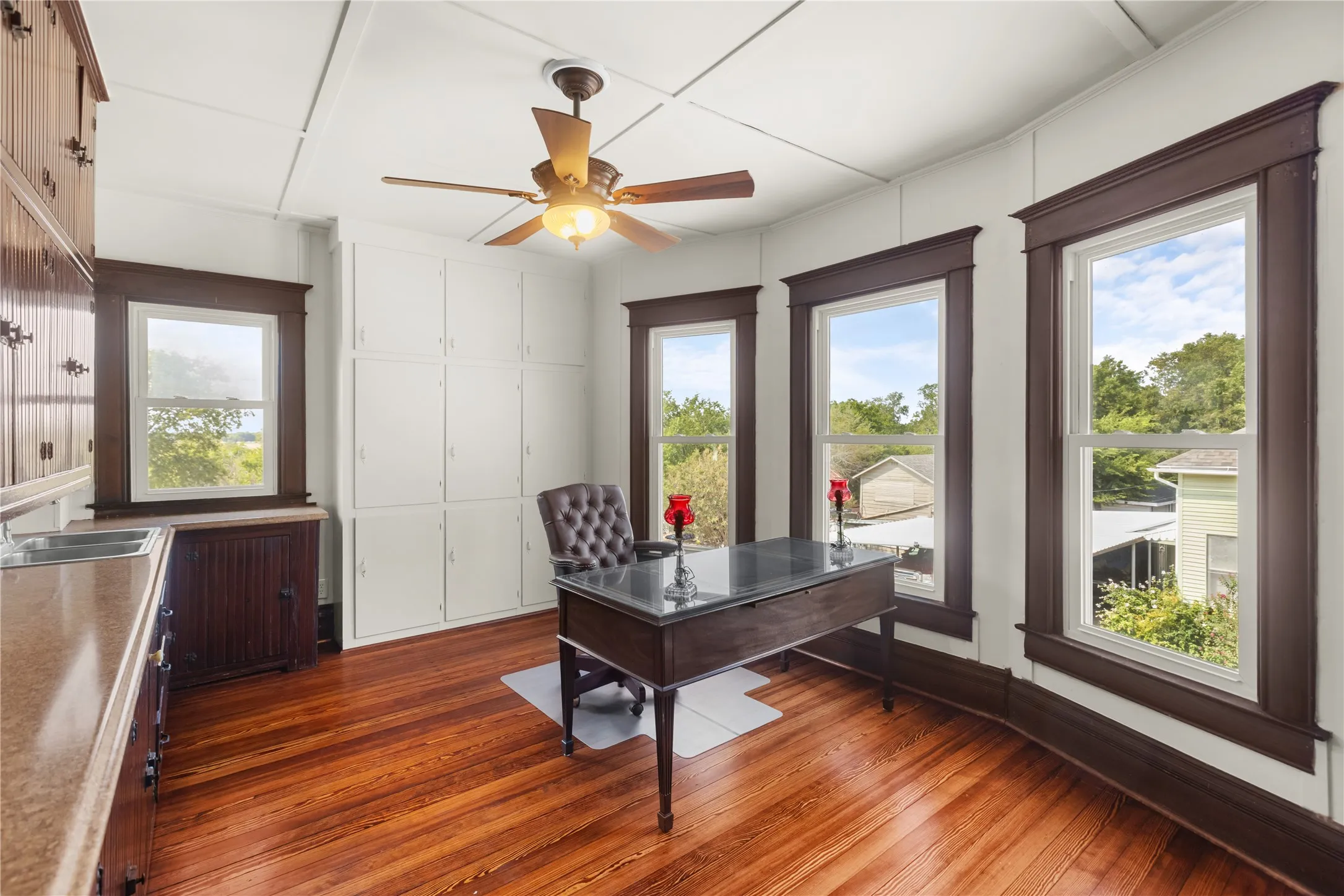 Hardwood flooring, multiple windows with dark wood trim, built-in cabinetry, ceiling fan, and built-in counter with sink